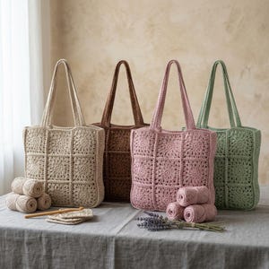 Può includere: Quattro borse tote all'uncinetto in beige, marrone, rosa antico e verde salvia, ciascuna composta da nove motivi quadrati. Le borse presentano due manici e sono esposte con gomitoli di lana abbinati e un uncinetto in legno su lino.