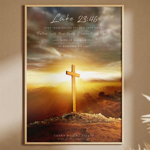 Op de afbeelding: Een ingelijste wandkunstprint met een houten kruis op een heuvel bij zonsondergang. De tekst luidt Luke 23:46, Then Jesus called out in a loud voice, Father, into Your hand, I commit My Spirit, and when He had said this, He breathed His last.