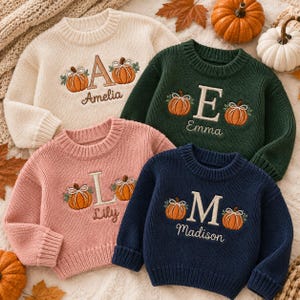 May include: Four long-sleeved knit sweaters in cream, dark green, dusty pink, and navy blue. Each sweater features an embroidered large capital letter, a name, and two orange pumpkins with white bows. The names are Amelia, Emma, Lily, and Madison.