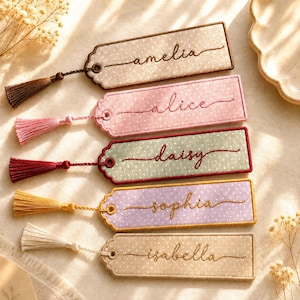 May include: Five rectangular fabric bookmarks with scalloped edges and white polka dots. Each bookmark features a unique name embroidered in cursive script: amelia, alice, daisy, sophia, and isabella. Each includes a matching tassel.