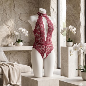 May include: A deep red lace bodysuit featuring a high neck collar, a plunging neckline with scalloped edges, and a cutout detail at the center of the leg opening. The garment is displayed on a white mannequin torso with intricate floral lace patterns.