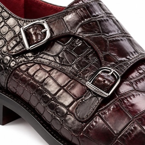 Close-up of croc embossed dark chocolate brown leather monk strap shoe with two polished silver buckles and detailed handcrafted stitching.