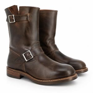 May include: A pair of dark brown leather mid-calf boots featuring a rounded toe, a stacked heel, and two silver-toned metal buckles. One buckle is positioned across the ankle, while the other is located at the top outer side. The word Velor is embossed on the heel.