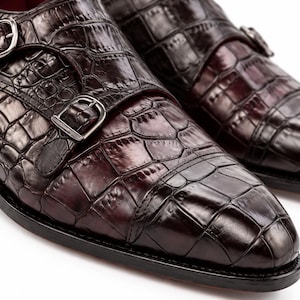 Close-up of dark brown crocodile embossed cap toe dress shoe showing glossy textured leather, double monk straps and refined toe construction.