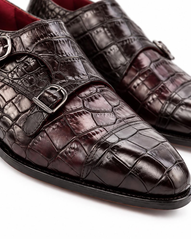 Close-up of dark brown crocodile embossed cap toe dress shoe showing glossy textured leather, double monk straps and refined toe construction.