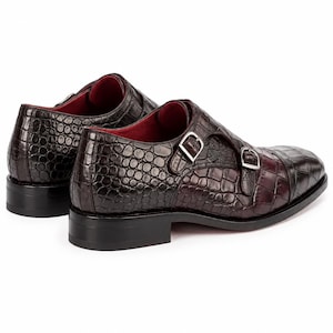 Rear side view of dark chocolate brown double monk strap dress shoes showing crocodile embossed leather, stacked heel and red leather lining.