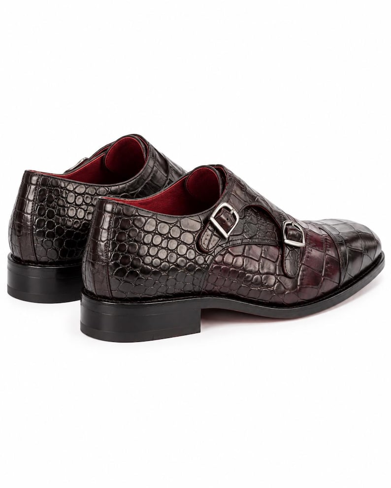 Rear side view of dark chocolate brown double monk strap dress shoes showing crocodile embossed leather, stacked heel and red leather lining.