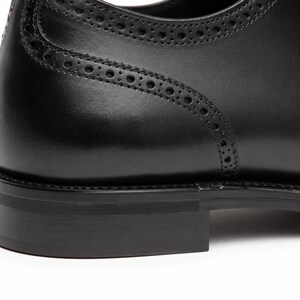Handmade men’s black Oxford dress shoes showing cap toe construction, lace-up design, low formal heel and refined dress-shoe build.