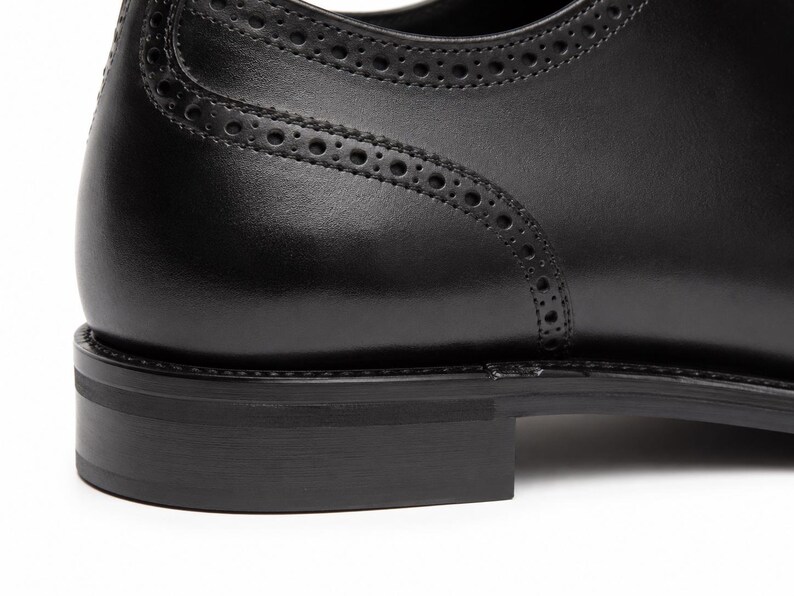 Handmade men’s black Oxford dress shoes showing cap toe construction, lace-up design, low formal heel and refined dress-shoe build.