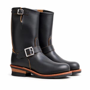 Könnte beinhalten: Ein Paar schwarze Leder-Ingenieurstiefel in Wadenhöhe mit silberfarbenen Metallschnallen am Knöchel und am Schaft, einer abgerundeten Zehenpartie sowie einem geschichteten Holzabsatz mit schwarzer Gummisohle und sichtbaren hellbraunen Lederkanten.