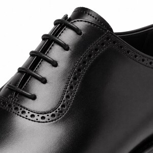 Close-up of black leather cap toe Oxford shoes showing smooth leather texture, precise stitching and handcrafted finishing.