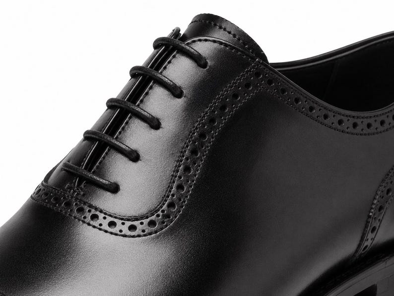 Close-up of black leather cap toe Oxford shoes showing smooth leather texture, precise stitching and handcrafted finishing.