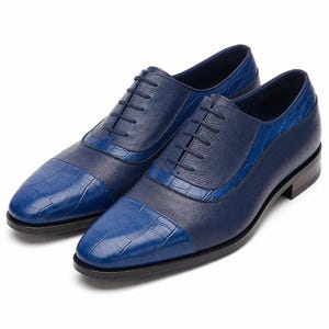 May include: A pair of blue oxford shoes featuring a combination of smooth textured leather and a glossy crocodile-embossed leather pattern on the toe cap, heel, and lace panel. The shoes include matching blue laces and a dark, low-profile heel.