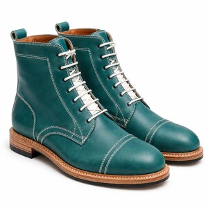 May include: A pair of teal leather lace-up boots featuring a cap toe design, white stitching details, white laces, and a stacked wooden heel with a black rubber sole. The boots have a pull tab at the heel and a smooth finish on the leather upper.