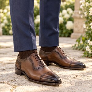 Men’s brown leather cap-toe Oxford shoes worn with navy suit trousers at an outdoor garden wedding, featuring dark burnished toes and brogue detailing.