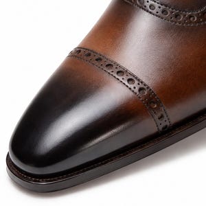 Three-quarter view of men’s brown Oxford shoes featuring dark burnished toe, cap toe design and refined brogue detailing.