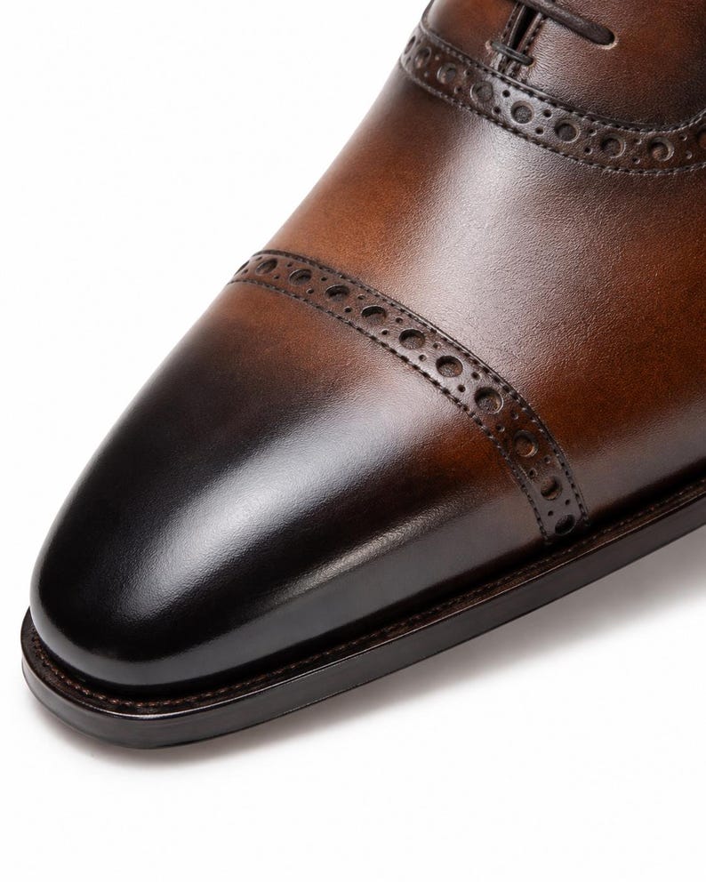 Three-quarter view of men’s brown Oxford shoes featuring dark burnished toe, cap toe design and refined brogue detailing.