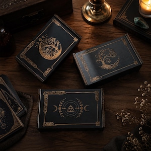 May include: Three rectangular black wooden boxes featuring intricate gold foil designs. The top left box displays a tree and moon phases, the top right shows a stylized tree, and the bottom box features a central triquetra symbol with moon phases.