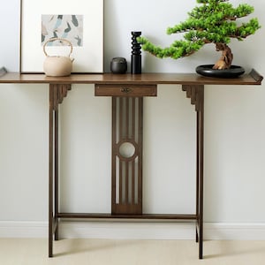 May include: A tall, narrow wooden console table with a single central drawer, featuring a slatted vertical support panel with a circular cutout. The table has flared ends on the top surface and decorative bracket supports under the tabletop.