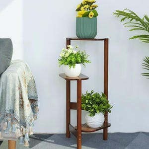 May include: A tall, three-tiered wooden plant stand with a dark brown finish. The stand features three shelves holding potted plants: a top shelf with a ribbed teal pot, a middle shelf with a white pot, and a bottom shelf with a white wavy pot.