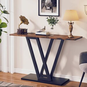 May include: A rectangular console table with a dark brown wood-grain finish top and a black metal base featuring two intersecting V-shaped legs connected to a solid rectangular floor plate. The table surface holds a gramophone, books, and a lamp.