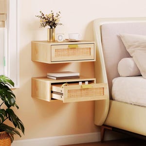 May include: Two light wood floating nightstands mounted on a wall, each featuring a single drawer with a woven cane front panel and a small gold handle. The top unit is closed, while the bottom unit is partially open, revealing internal contents.