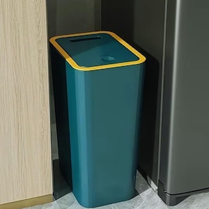 Può includere: Un cestino per i rifiuti alto e rettangolare con un corpo color verde ottanio profondo e un bordo giallo brillante a contrasto attorno al coperchio superiore. Il coperchio presenta un'apertura rettangolare e un incavo circolare.