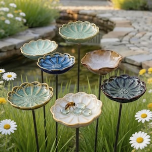 May include: A collection of seven ceramic flower-shaped garden stakes on thin metal rods. The bowls feature scalloped edges and varied glazed finishes in shades of blue, green, white, and brown. One white bowl contains a bee and glass beads.