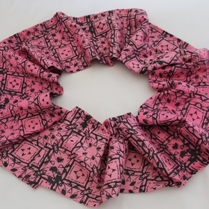 May include: Pink fabric scarf with a black geometric pattern. The scarf is folded in a circle.