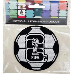 May include: A black and white soccer ball patch with a FIFA trophy design. The patch is round and features the FIFA logo. The packaging reads "OFFICIAL LICENSED PRODUCT". A gold-colored pin with a FIFA trophy is also included.