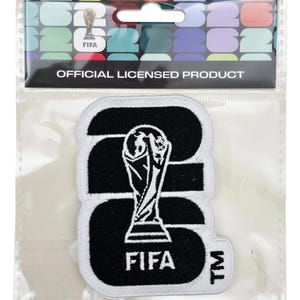 May include: A black and white FIFA patch in a clear plastic package. The patch features the FIFA trophy and the word "FIFA". The packaging reads "OFFICIAL LICENSED PRODUCT".