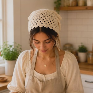 May include: A cream-colored crochet headscarf featuring a repeating openwork square pattern and a scalloped edge. The headscarf is tied at the back with two thin matching crochet strings, creating a triangular shape that covers the top of the head.