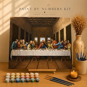 Peut inclure: Un kit de peinture par numéros représentant une reproduction de La Cène sur toile. L'ensemble comprend une palette numérotée avec vingt et un petits pots de peinture, trois pinceaux et un chevalet en bois. Le texte indique PAINT BY NUMBERS KIT.