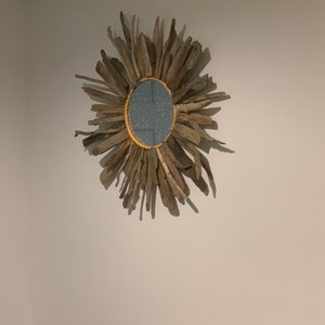 May include: A round mirror with a gold frame surrounded by driftwood branches. The mirror has a blue background with a glittery texture.
