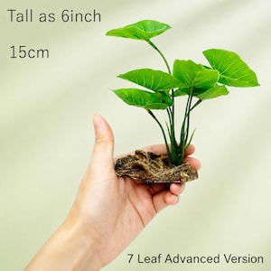 May include: An artificial green plant with seven leaves attached to a textured brown rock base. The plant is 6 inches tall. Text on the image reads: Tall as 6inch, 15cm, 7 Leaf Advanced Version.