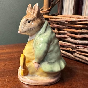 May include: A ceramic figurine of a rabbit in profile, featuring a brown head, a light green jacket with a subtle crackle glaze finish, and a yellow waistcoat. The rabbit is depicted in a seated position on a circular base with a glossy finish.