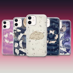 May include: Five clear smartphone cases featuring celestial designs with white rabbits, moons, and stars. The designs include purple, dark blue, and cream backgrounds with various artistic illustrations of rabbits in space-themed settings.