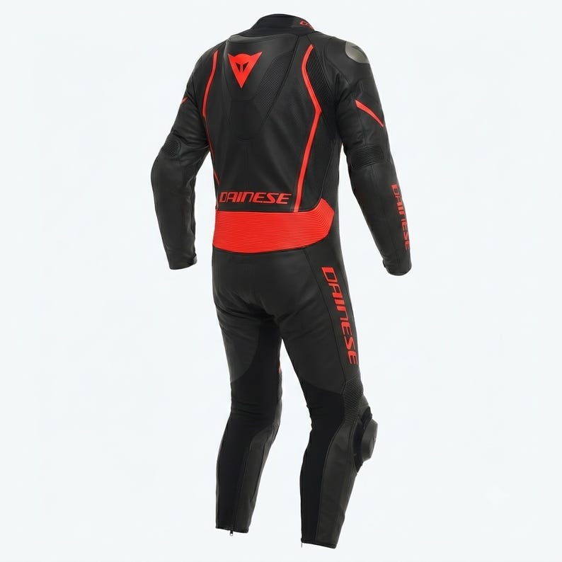 Puede incluir: Traje de carreras de motociclismo negro y rojo. El traje presenta una base negra con detalles rojos en los hombros, la espalda y las piernas. El logotipo de Dainese es visible en la espalda y los brazos. Acolchado protector en rodillas y codos.