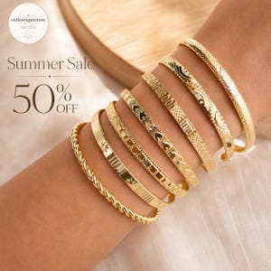 Könnte beinhalten: Ein Set aus sieben goldfarbenen Metallarmreifen am Handgelenk. Die Armbänder weisen verschiedene Texturen und Muster auf, darunter ein gedrehtes Seildesign, Sternmotive, geometrische Formen, Herzausschnitte und eingravierte Mondsicheln.