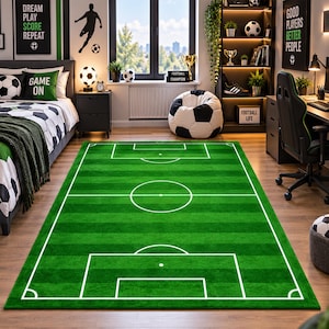 May include: A rectangular area rug featuring a vibrant green football pitch design with white painted boundary lines, a centre circle, and goal boxes. The rug mimics the appearance of a grass pitch with alternating light and dark green stripes.