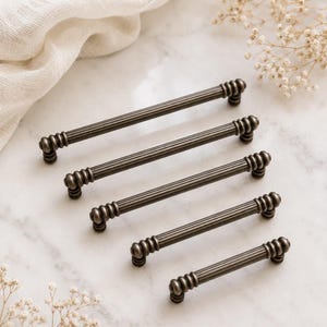 May include: Five dark bronze-toned metal drawer pulls arranged in a diagonal line. Each handle features a long, cylindrical, ribbed center section with decorative, multi-ringed circular accents at both ends and small mounting posts underneath.