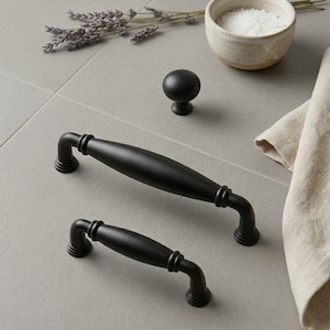 May include: Two matte black metal cabinet pulls of different lengths and one matching round cabinet knob. The hardware features a smooth, curved design with tiered circular bases at each connection point, presented in a clean, organized arrangement.