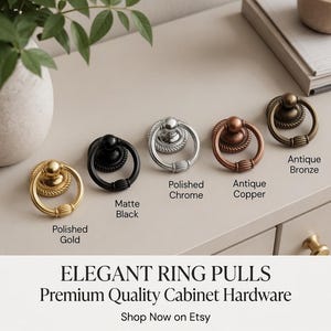 Puede incluir: Una selección de elegantes tiradores de anillo en oro pulido, negro mate, cromo pulido, cobre antiguo y bronce antiguo. Los tiradores se muestran sobre una superficie clara, destacando su diseño. El texto dice "Elegant Ring Pulls, Premium Quality Cabinet Hardware."