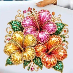 Puede incluir: Un lienzo cuadrado blanco con un vibrante diseño de arte de diamantes de tres grandes flores de hibisco en tonos rosa brillante, amarillo dorado y naranja, acentuado con hojas verdes brillantes y complejos remolinos dorados.