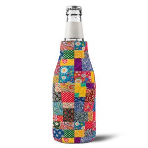 Op de afbeelding: Een glazen fles in een stoffen hoes met een levendig, veelkleurig patchworkontwerp. De hoes toont diverse patronen, waaronder bloemmotieven, paisley-prints en stippen in de kleuren rood, blauw, geel en groen.