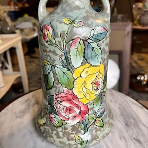 May include: A ceramic vase with two handles featuring a mottled sage green and grey background. The surface is decorated with a hand-painted floral design of a large yellow rose, a large pink rose, and green leaves with thin black outlines.