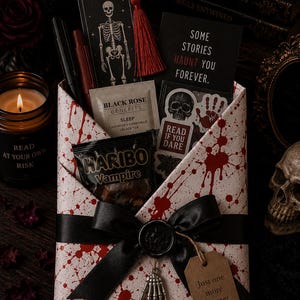 May include: A white envelope with red blood splatter patterns, tied with a black ribbon, a black wax seal, and a silver skeleton hand charm. It contains a skeleton bookmark with a red tassel, a tea bag, Haribo Vampire candy, and stickers.