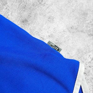May include: A close-up of a blue athletic garment with white trim. The tag reads "CLIMALITE" in white text on a grey background. The fabric is a vibrant blue.