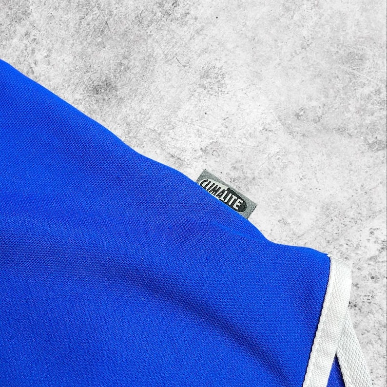 May include: A close-up of a blue athletic garment with white trim. The tag reads "CLIMALITE" in white text on a grey background. The fabric is a vibrant blue.