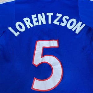 May include: Royal blue jersey with the name "LORENTZSON" in white block letters across the upper back. A large white number "5" with a red outline is centered below the name. The jersey is made of a breathable fabric.